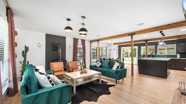 living area with visible vents, beam ceiling, a wood stove, and light wood finished floors