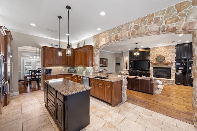 kitchen with a ceiling fan, a peninsula, arched walkways, a sink, and stainless steel dishwasher