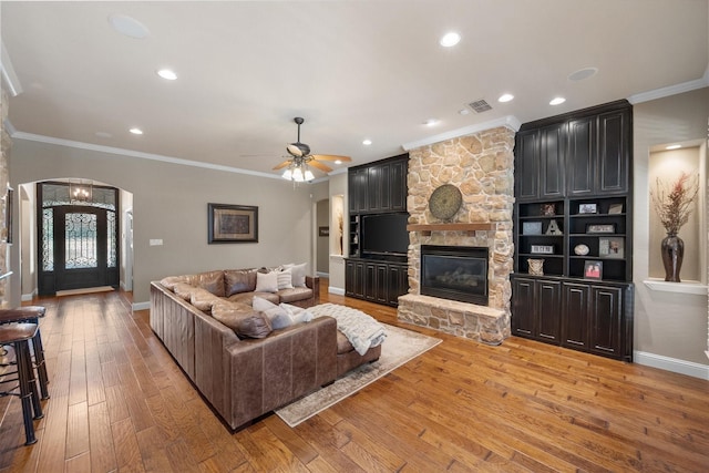 living area with visible vents, light wood finished floors, a fireplace, arched walkways, and crown molding