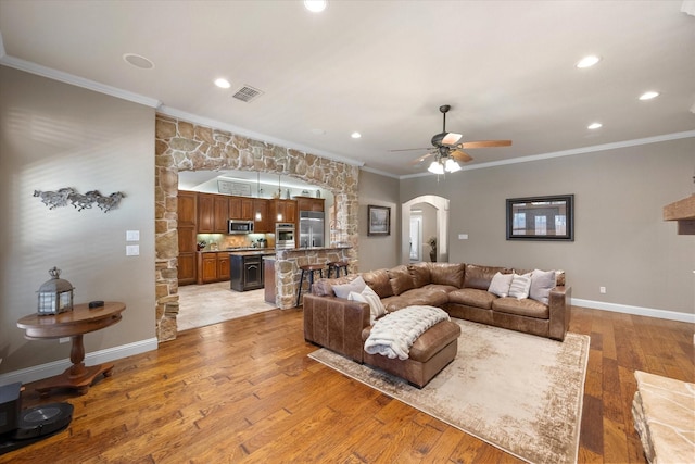 living room with visible vents, light wood finished floors, arched walkways, ceiling fan, and crown molding