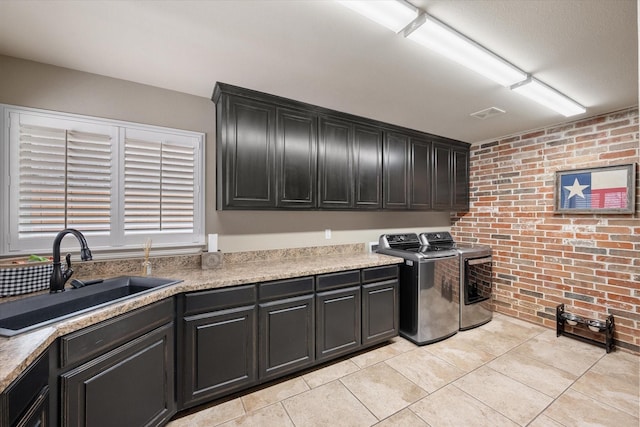 washroom with a sink, cabinet space, brick wall, light tile patterned floors, and washing machine and clothes dryer