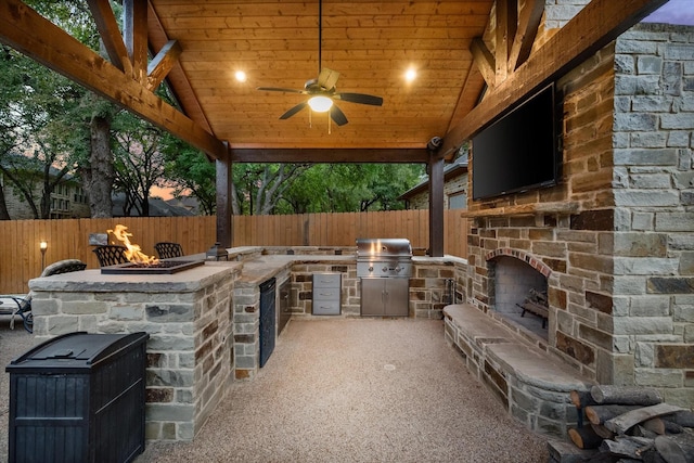 view of patio with grilling area, an outdoor stone fireplace, an outdoor kitchen, and fence