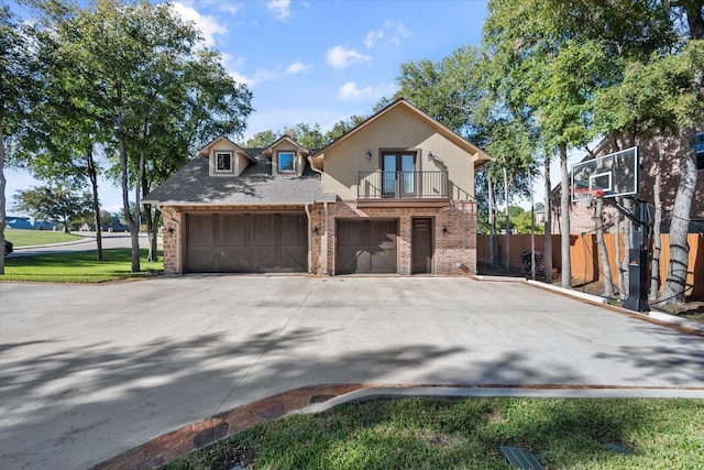 view of front of property with stucco siding, driveway, a balcony, french doors, and brick siding