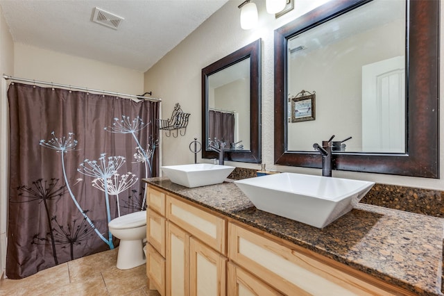 bathroom with a sink, visible vents, toilet, and double vanity