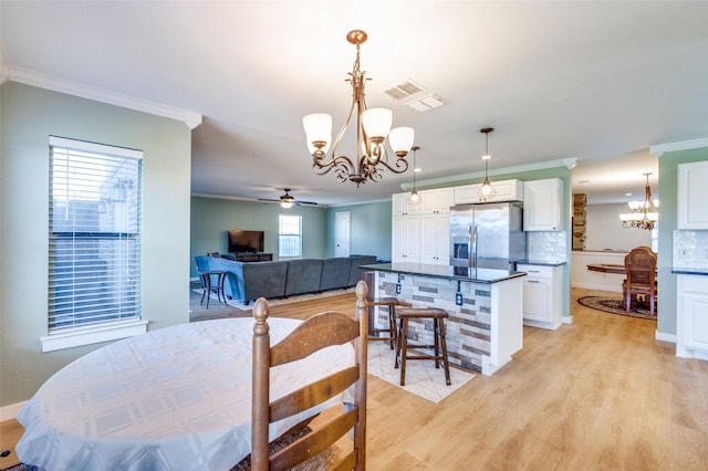 dining room featuring visible vents, ceiling fan with notable chandelier, crown molding, and light wood finished floors