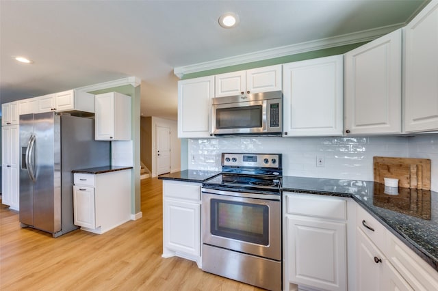 kitchen featuring light wood finished floors, decorative backsplash, dark stone countertops, appliances with stainless steel finishes, and white cabinetry