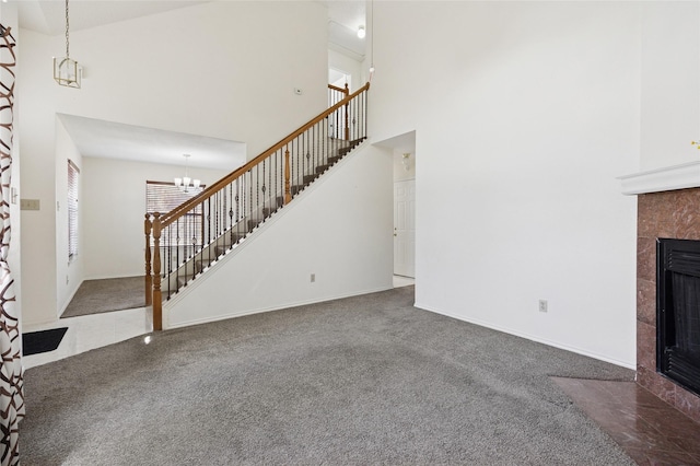 unfurnished living room featuring stairway, an inviting chandelier, a tile fireplace, a towering ceiling, and carpet flooring