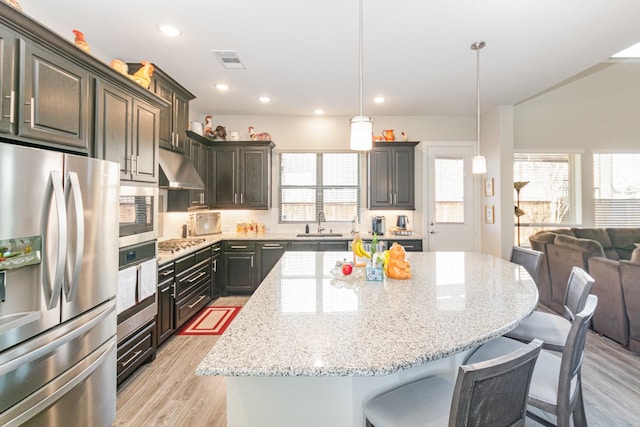 kitchen featuring visible vents, a breakfast bar, stainless steel appliances, under cabinet range hood, and a center island