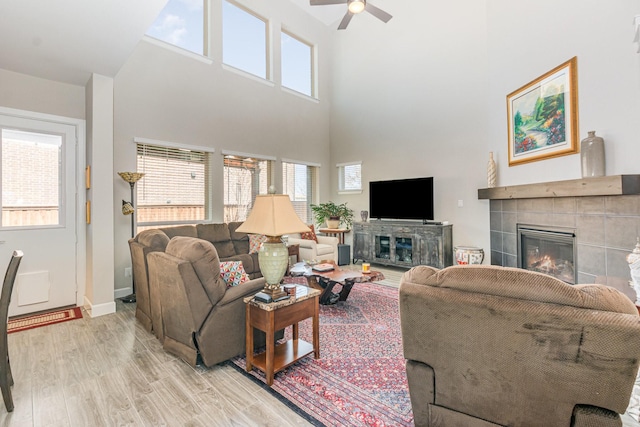 living area with a tiled fireplace, ceiling fan, baseboards, and light wood-style floors