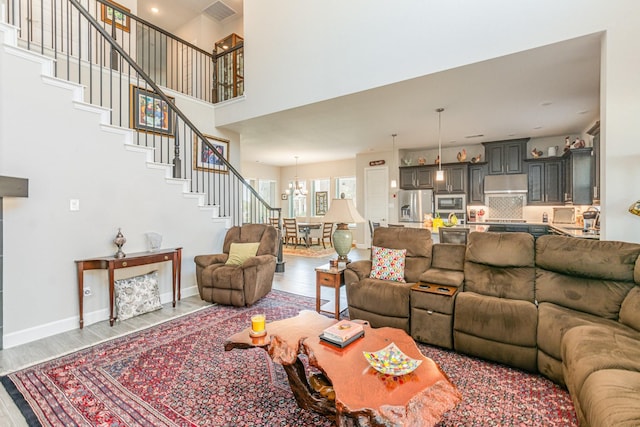 living room with a notable chandelier, wood finished floors, a high ceiling, baseboards, and stairs