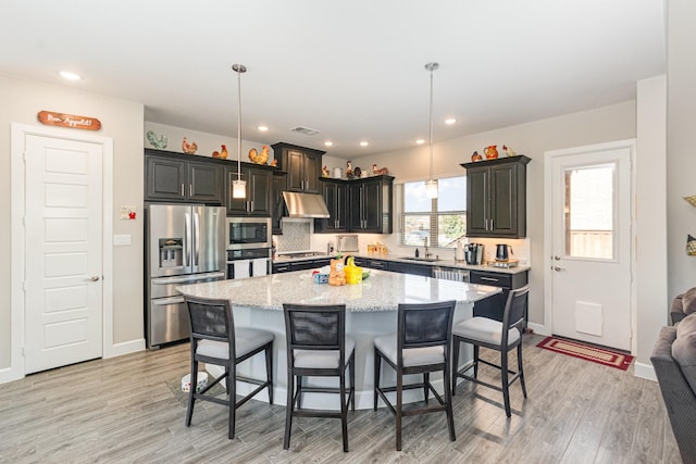 kitchen featuring visible vents, under cabinet range hood, a breakfast bar, light wood-style flooring, and appliances with stainless steel finishes