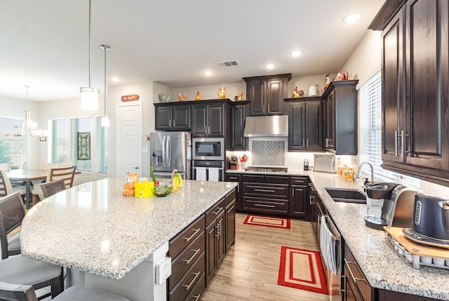 kitchen with under cabinet range hood, decorative backsplash, appliances with stainless steel finishes, light wood-style floors, and a sink