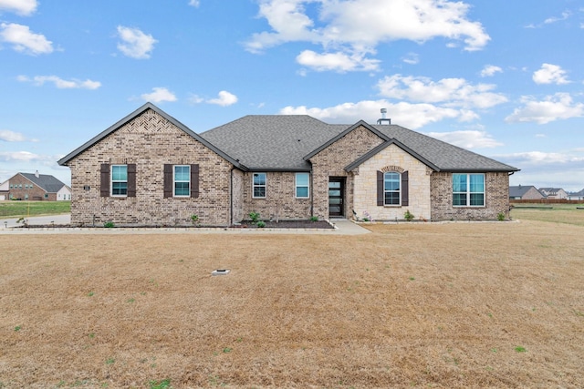 french provincial home featuring stone siding, brick siding, roof with shingles, and a front yard