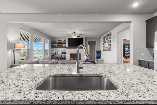 kitchen featuring light stone counters, open floor plan, a fireplace, and a sink