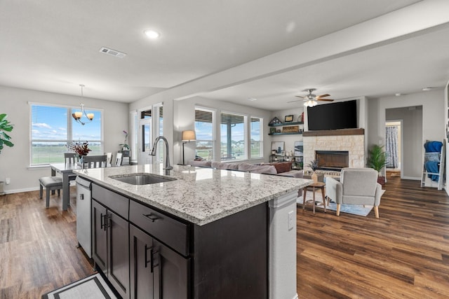 kitchen with light stone countertops, visible vents, dark wood finished floors, a sink, and a stone fireplace