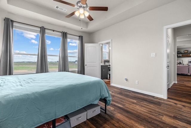 bedroom featuring visible vents, a ceiling fan, a tray ceiling, dark wood-style floors, and baseboards