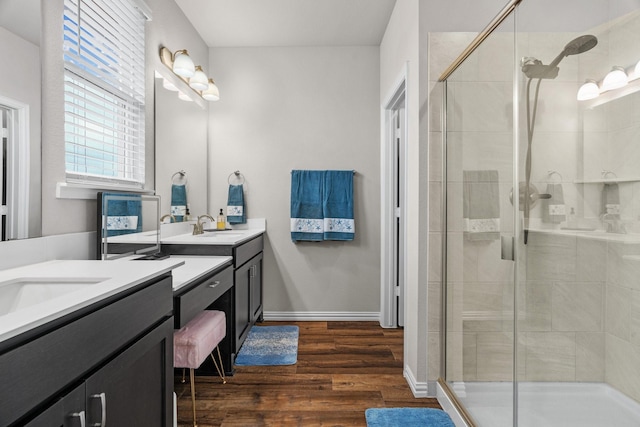 bathroom with two vanities, a sink, wood finished floors, a shower stall, and baseboards