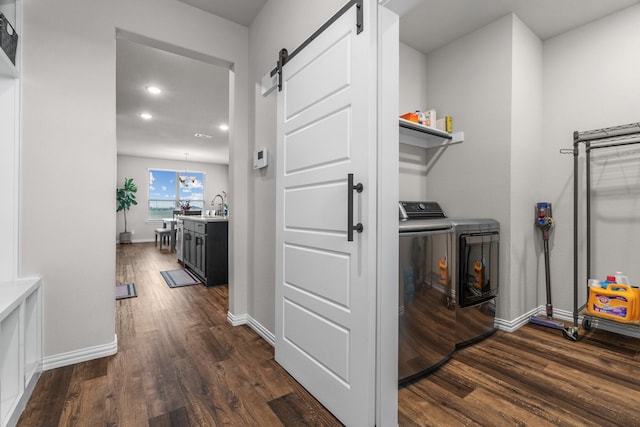 clothes washing area with a barn door, dark wood-style flooring, washing machine and dryer, and laundry area