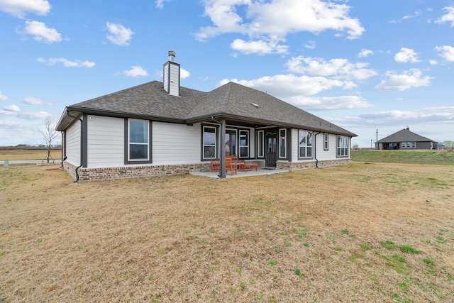 rear view of property featuring brick siding, a shingled roof, a chimney, a yard, and a patio area
