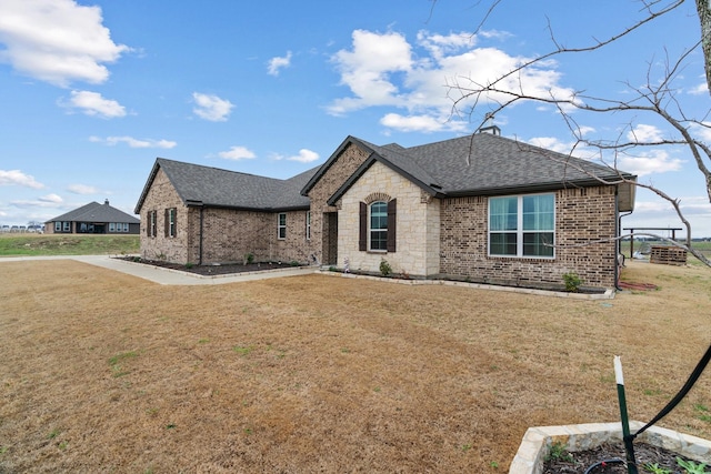 french country home featuring a front lawn, stone siding, brick siding, and roof with shingles