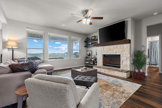 living room featuring visible vents, a ceiling fan, wood finished floors, a stone fireplace, and baseboards