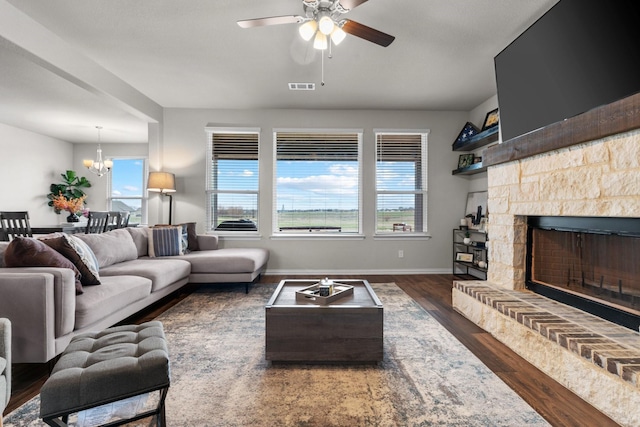 living room featuring wood finished floors, visible vents, baseboards, a fireplace with raised hearth, and ceiling fan with notable chandelier
