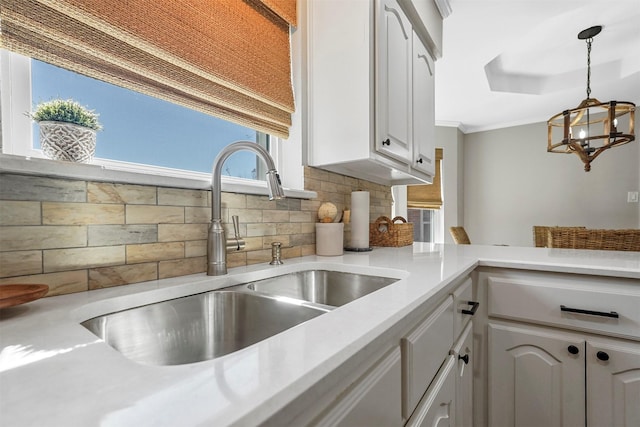 kitchen with a sink, white cabinets, light countertops, decorative backsplash, and hanging light fixtures