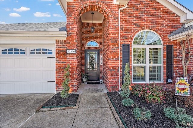 entrance to property with an attached garage, brick siding, and roof with shingles