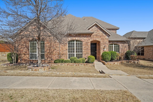 french country style house with brick siding and a shingled roof