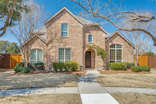 view of front of property featuring brick siding, a shingled roof, and fence