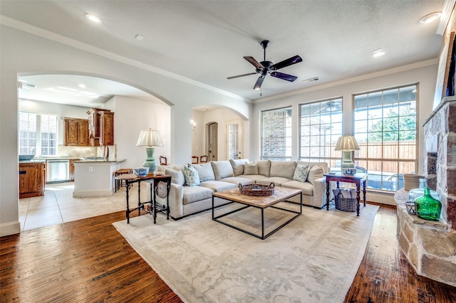 living room featuring a ceiling fan, recessed lighting, arched walkways, crown molding, and light wood finished floors