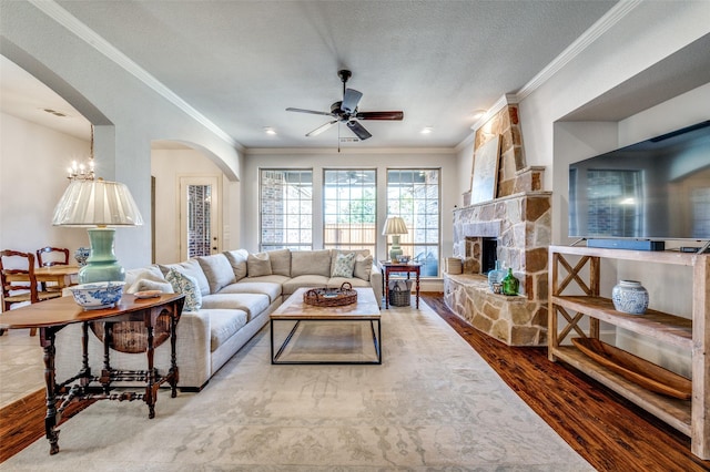 13508 Lampton Cir SE, Frisco, TX 75035 - living room with a ceiling fan, wood finished floors, arched walkways, a stone fireplace, and ornamental molding