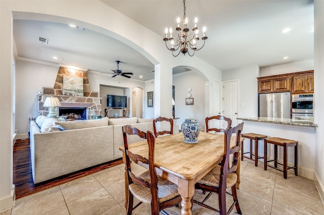 dining room with ornamental molding, a ceiling fan, arched walkways, a fireplace, and baseboards