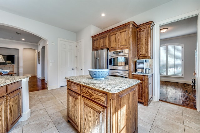 13508 Lampton Cir SE, Frisco, TX 75035 - kitchen with appliances with stainless steel finishes, brown cabinets, arched walkways, crown molding, and light tile patterned floors