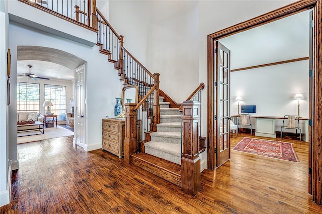 entryway featuring hardwood / wood-style floors, arched walkways, stairs, french doors, and a towering ceiling