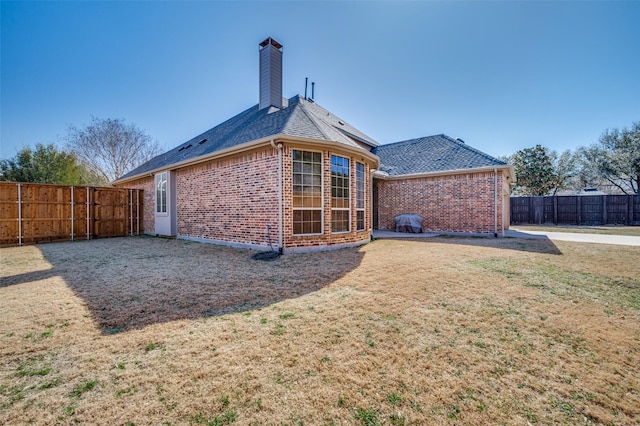 back of property with a lawn, a fenced backyard, roof with shingles, brick siding, and a chimney