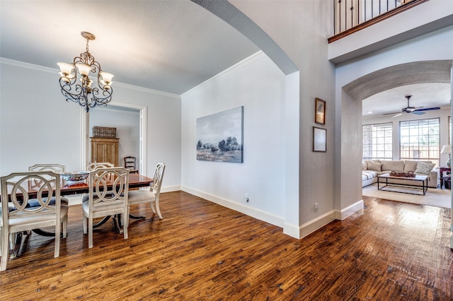 dining space featuring baseboards, ornamental molding, ceiling fan with notable chandelier, arched walkways, and wood-type flooring