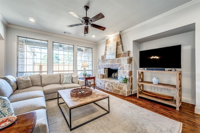 living room with visible vents, wood finished floors, a fireplace, crown molding, and ceiling fan