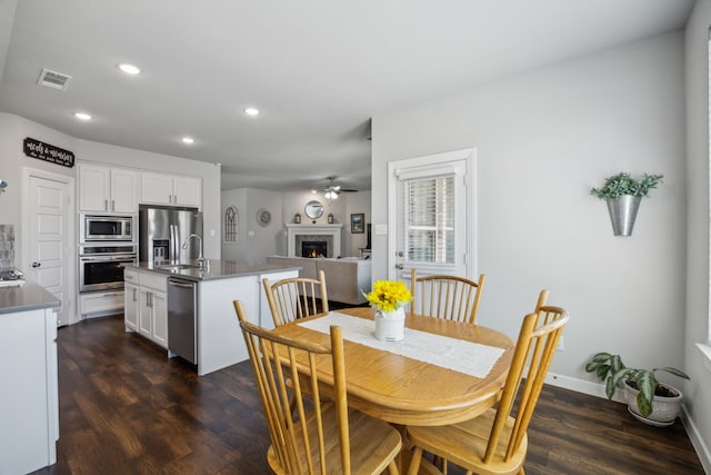 dining room featuring visible vents, a warm lit fireplace, dark wood finished floors, recessed lighting, and baseboards