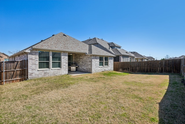 rear view of property with a lawn, roof with shingles, a fenced backyard, and brick siding