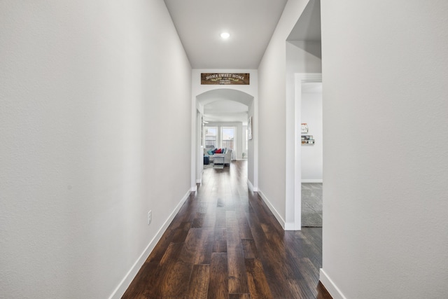 hall with baseboards, arched walkways, and dark wood-style flooring