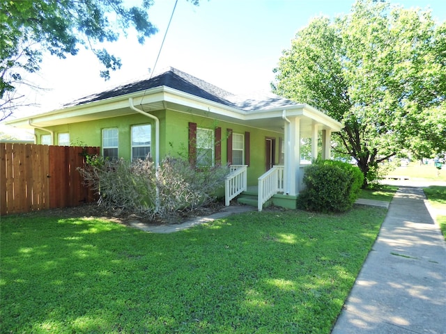 view of home's exterior with stucco siding, a lawn, a porch, fence, and a shingled roof