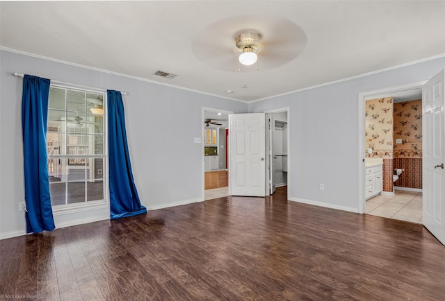 unfurnished bedroom featuring visible vents, crown molding, baseboards, ensuite bathroom, and wood finished floors