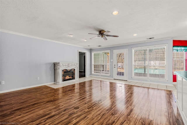 unfurnished living room featuring visible vents, crown molding, light wood-style flooring, a glass covered fireplace, and a textured ceiling