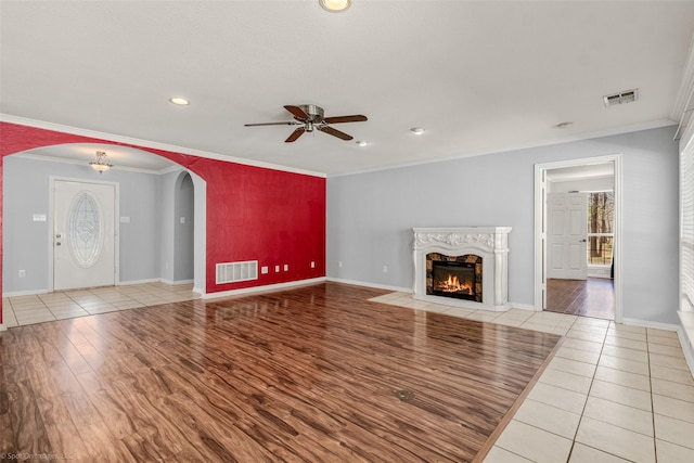 unfurnished living room featuring visible vents, arched walkways, light wood-style floors, crown molding, and a premium fireplace