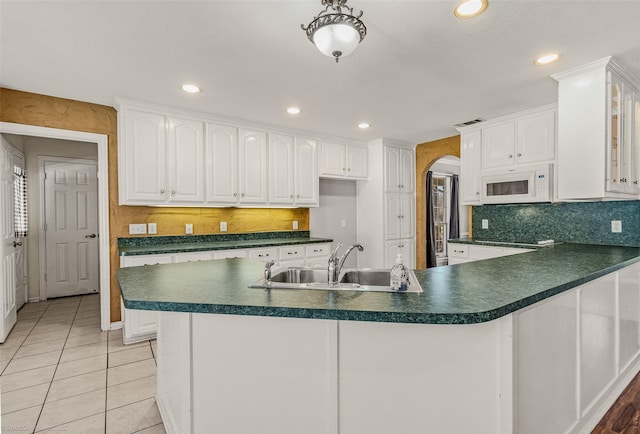 kitchen featuring a sink, dark countertops, white cabinetry, arched walkways, and white microwave