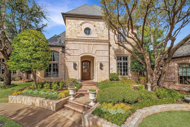 french country inspired facade featuring stone siding and roof with shingles