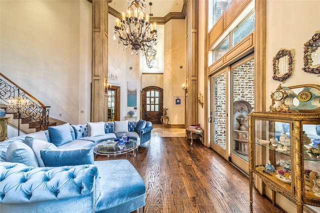 living room with dark wood-style floors, an inviting chandelier, crown molding, a towering ceiling, and stairs