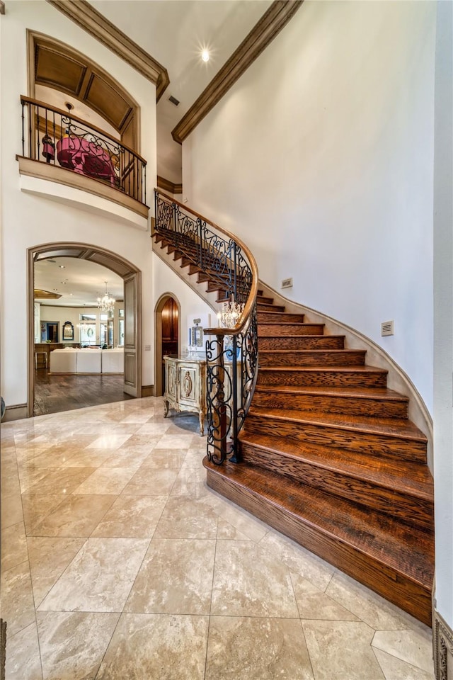 stairs featuring visible vents, a chandelier, ornamental molding, a high ceiling, and arched walkways