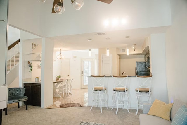 kitchen featuring visible vents, a peninsula, freestanding refrigerator, light carpet, and a kitchen breakfast bar